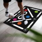 Person playing with a soccer ball on a patterned exercise mat indoors.