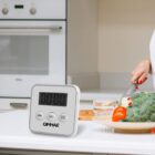 Digital timer on kitchen counter; person chopping vegetables in the background.