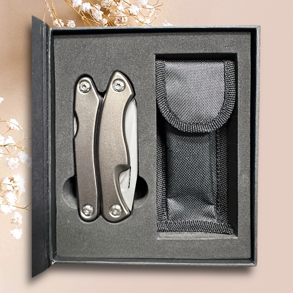 Gift box featuring a multitool and pouch, set against a beige background with flowers.