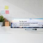 Desk with to-do list plaque, pen, plant, and sticky notes on wall.
