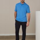 A man wearing a blue polo shirt and black pants standing indoors with a neutral expression.