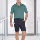 Man in teal shirt and black shorts standing in a bright corridor.
