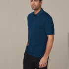 Man in a blue polo shirt and black shorts stands against a plain background.
