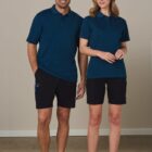 Man and woman in navy polo shirts and black shorts, standing and smiling.