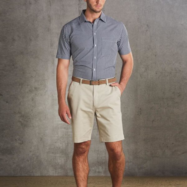 Man in checkered shirt and khaki shorts standing against a gray background.