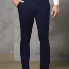 Man in white shirt and navy trousers stands against a textured backdrop.