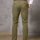 Person in olive green pants, white shirt, and brown belt, standing against a gray wall.