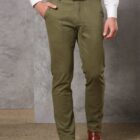 Man in olive green pants, white shirt, brown belt, and shoes, standing with one hand in pocket.