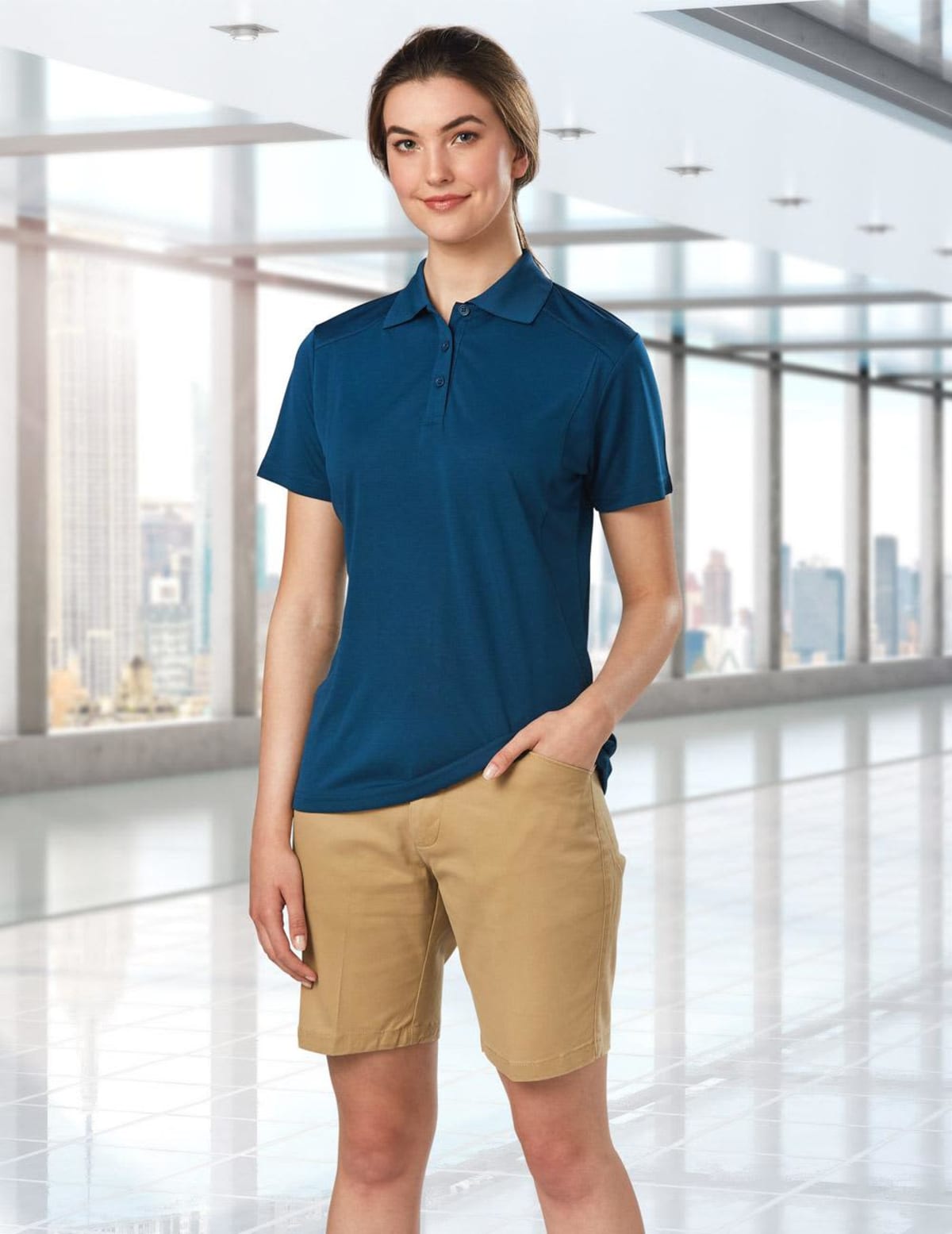A person in a blue polo shirt and khaki shorts stands in a modern, spacious building.