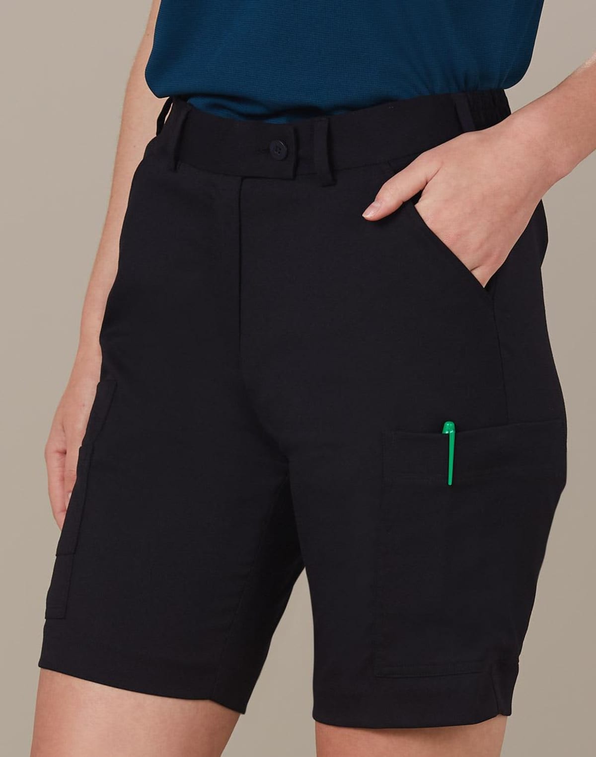 Person wearing black utility shorts with hands in pockets and a green pen visible.