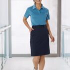 Person in blue polo and dark skirt smiling, walking indoors with bright background.