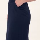 Person in a dark blue skirt with hand in pocket, standing against a plain background.