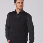 Man in a dark outfit with a V-neck sweater, looking to the side against a light background.