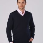 Man in a black V-neck sweater and pink shirt poses against a plain background.