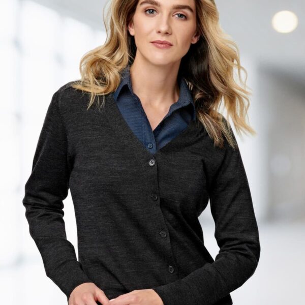 Person in a dark cardigan and blue shirt stands in a bright, blurred indoor setting.