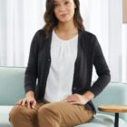 Person sitting on a couch wearing a cardigan, white blouse, and khaki pants.