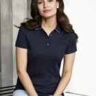 Woman with long brown hair wearing a navy polo shirt and light jeans, sitting indoors.