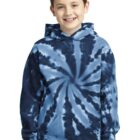 Boy wearing a blue tie-dye hoodie, smiling, with hands in pocket, standing against a plain backdrop.