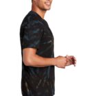 Person in a tie-dye shirt and jeans smiling against a white background.