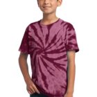 Boy wearing a maroon tie-dye shirt and jeans smiles with hand in pocket.