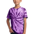 Boy in a purple tie-dye shirt and jeans, smiling with hands in pockets.
