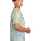 Boy in tie-dye shirt and jeans, standing and looking to the side against a white background.