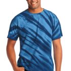 Man in a blue tie-dye shirt smiles with hands in pockets.