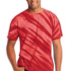 Man smiling, wearing a red tie-dye t-shirt and dark jeans, with one hand in pocket.