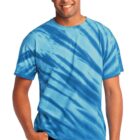Man wearing a blue tie-dye shirt, smiling, with one hand in pocket.