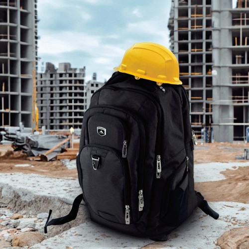 Black backpack and safety helmet at a construction site with buildings in the background.