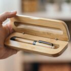 A hand holding an open bamboo case with a pen inside.