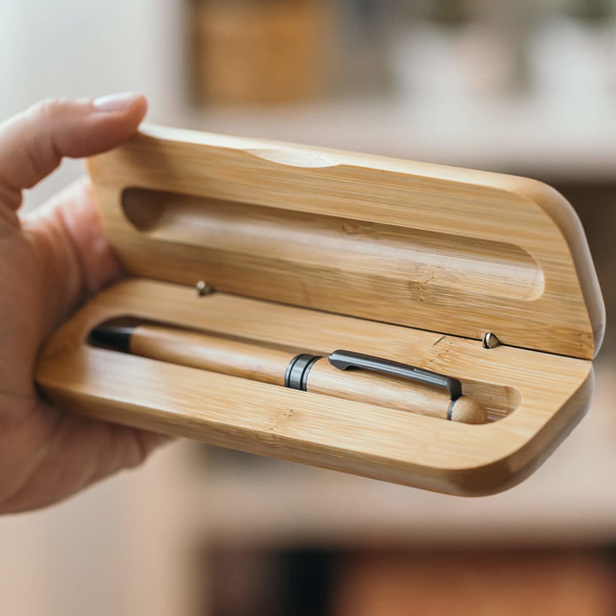 A hand holding an open bamboo case with a pen inside.