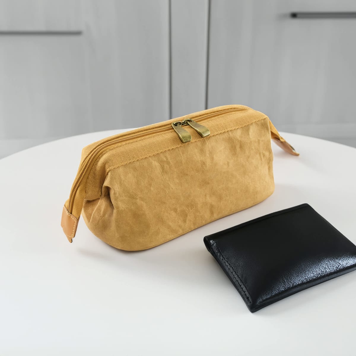 A yellow zippered pouch and a black wallet on a white table.