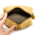 A hand holds open an empty tan zipper pouch on a white background.