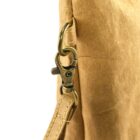Close-up of a brass clasp attaching a tan strap to a tan leather bag.