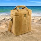 Tan insulated cooler bag on sandy beach with ocean waves and blue sky in the background.