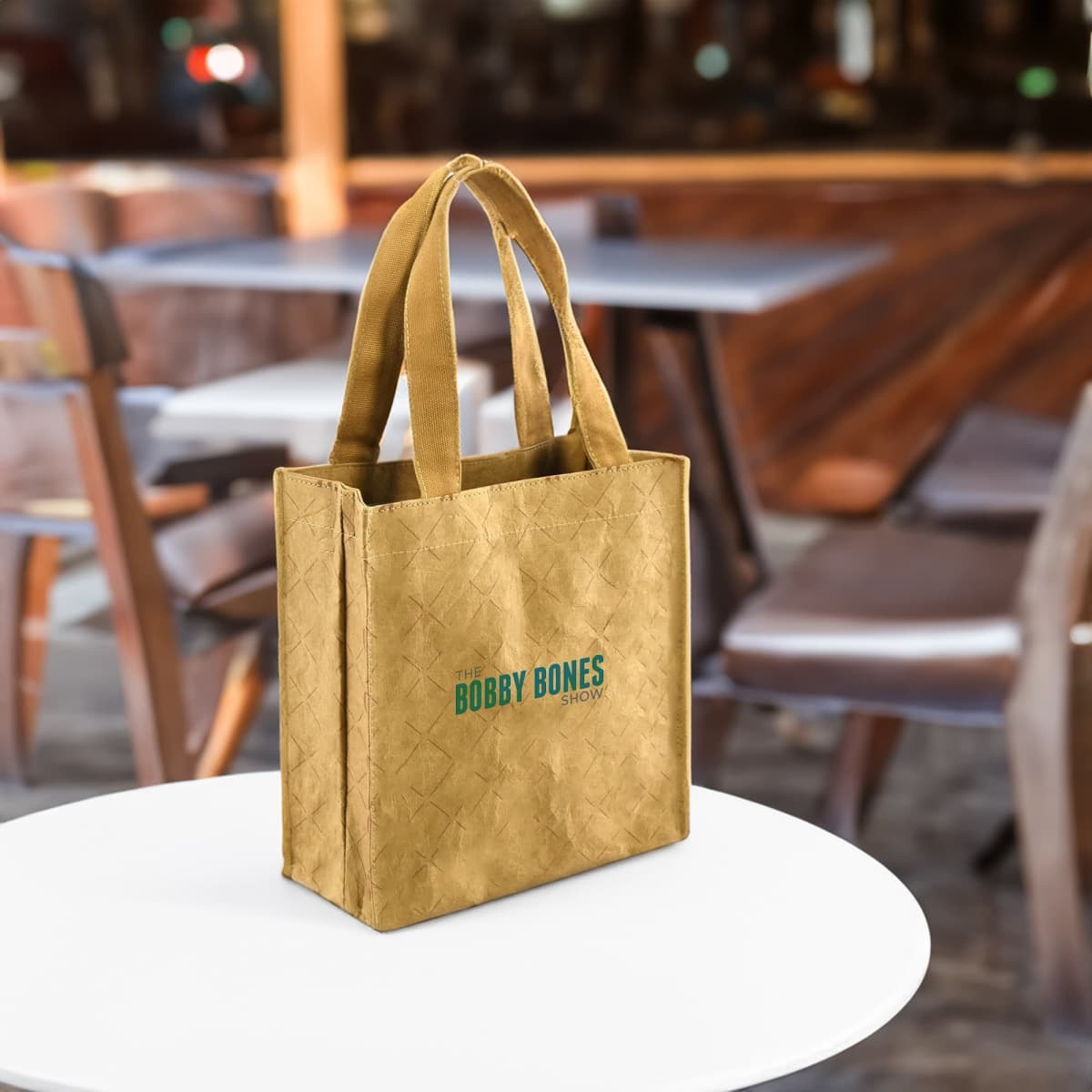 Tan tote bag with The Bobby Bones Show text sits on a white table in a cafe setting.