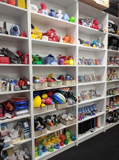 White shelves filled with colorful toys, art supplies, books, and promotional gifts for kids.