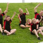 Group of five people in red and black sportswear cheering on grassy hill.