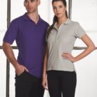 A man in a purple polo and a woman in a gray polo stand indoors.