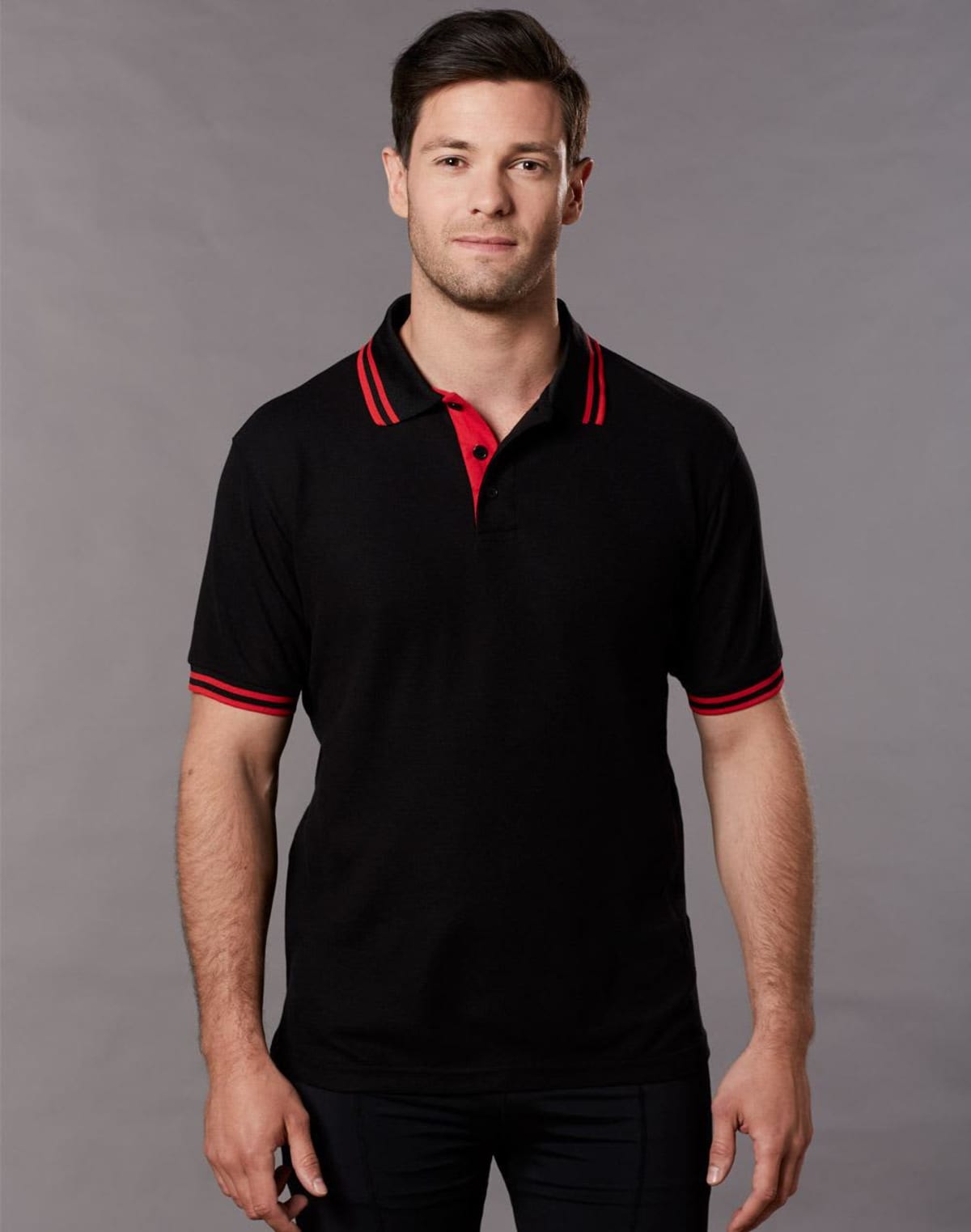 Man in black polo shirt with red accents standing against a grey background.
