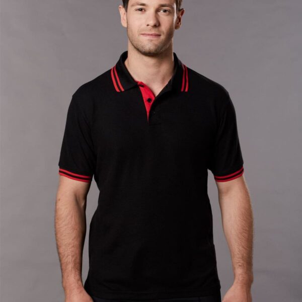 Man in black polo shirt with red accents, standing in front of a gray background.