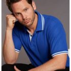 Man in a blue polo shirt with white stripes, sitting and resting his head on his hand.