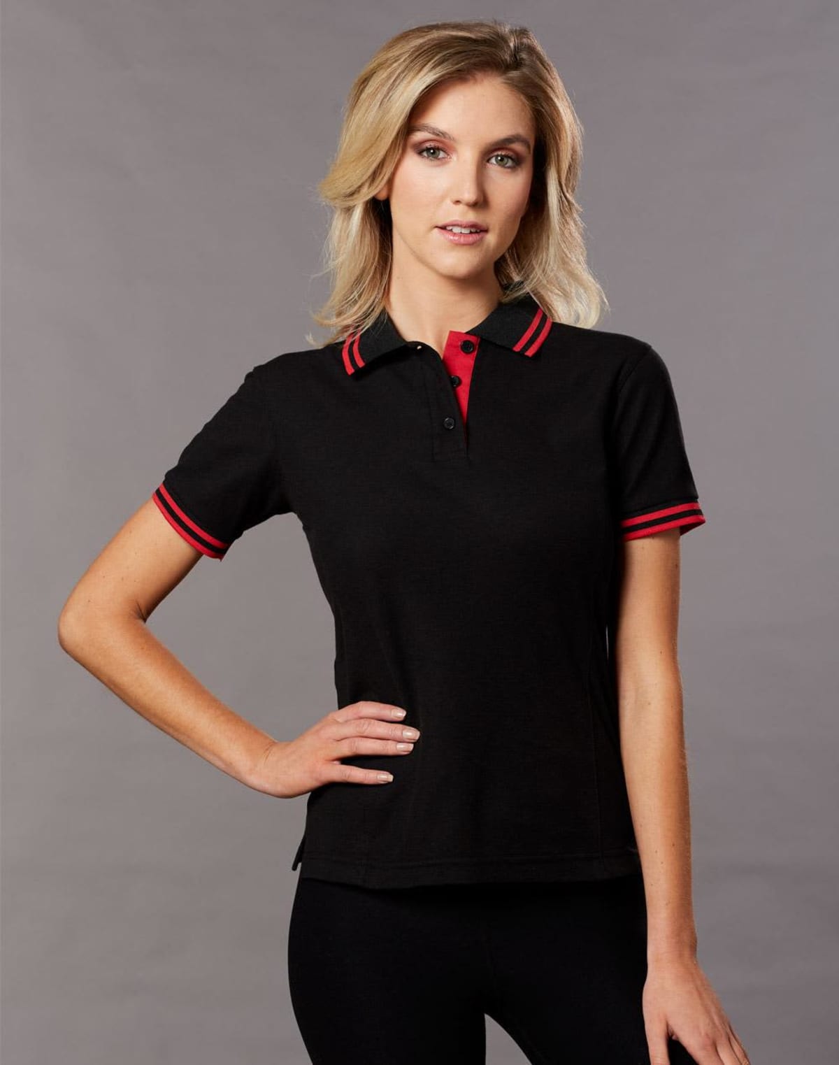 Woman in black polo shirt with red accents posing confidently against a gray background.