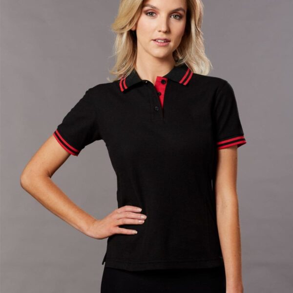 Person in a black polo shirt with red trim poses against a gray background.