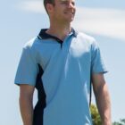 Man in a light blue polo shirt outdoors, smiling against a blue sky backdrop.