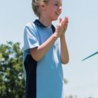 Child clapping outdoors in a blue shirt.