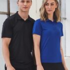 Two people in polo shirts, one black and one blue, standing indoors.