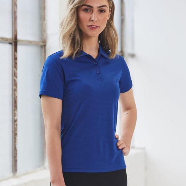 Person in a blue polo shirt standing indoors by a window.