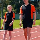 Two people in orange and black outfits walking on a track outdoors.